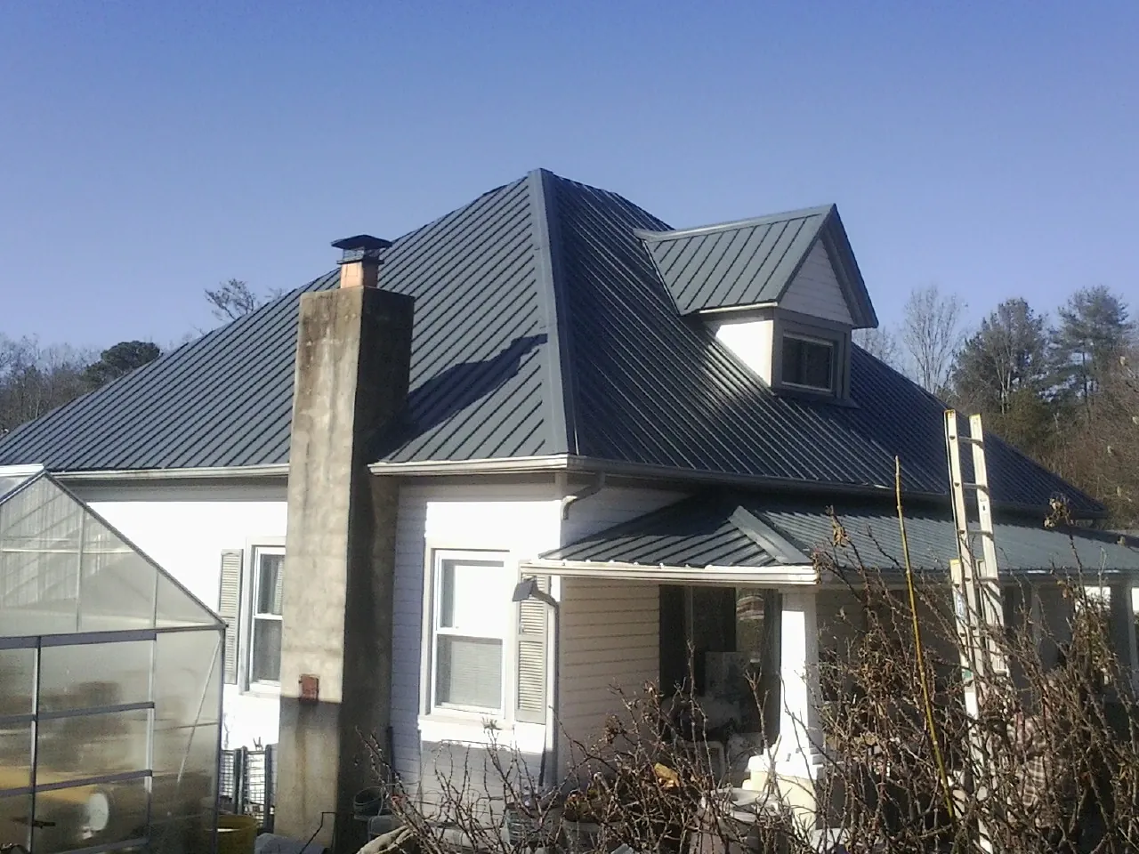 Dark blue standing seam metal roof on a white farmhouse with dormer — Slate & Tile Roof Repair by Roofing Brothers in Hammett