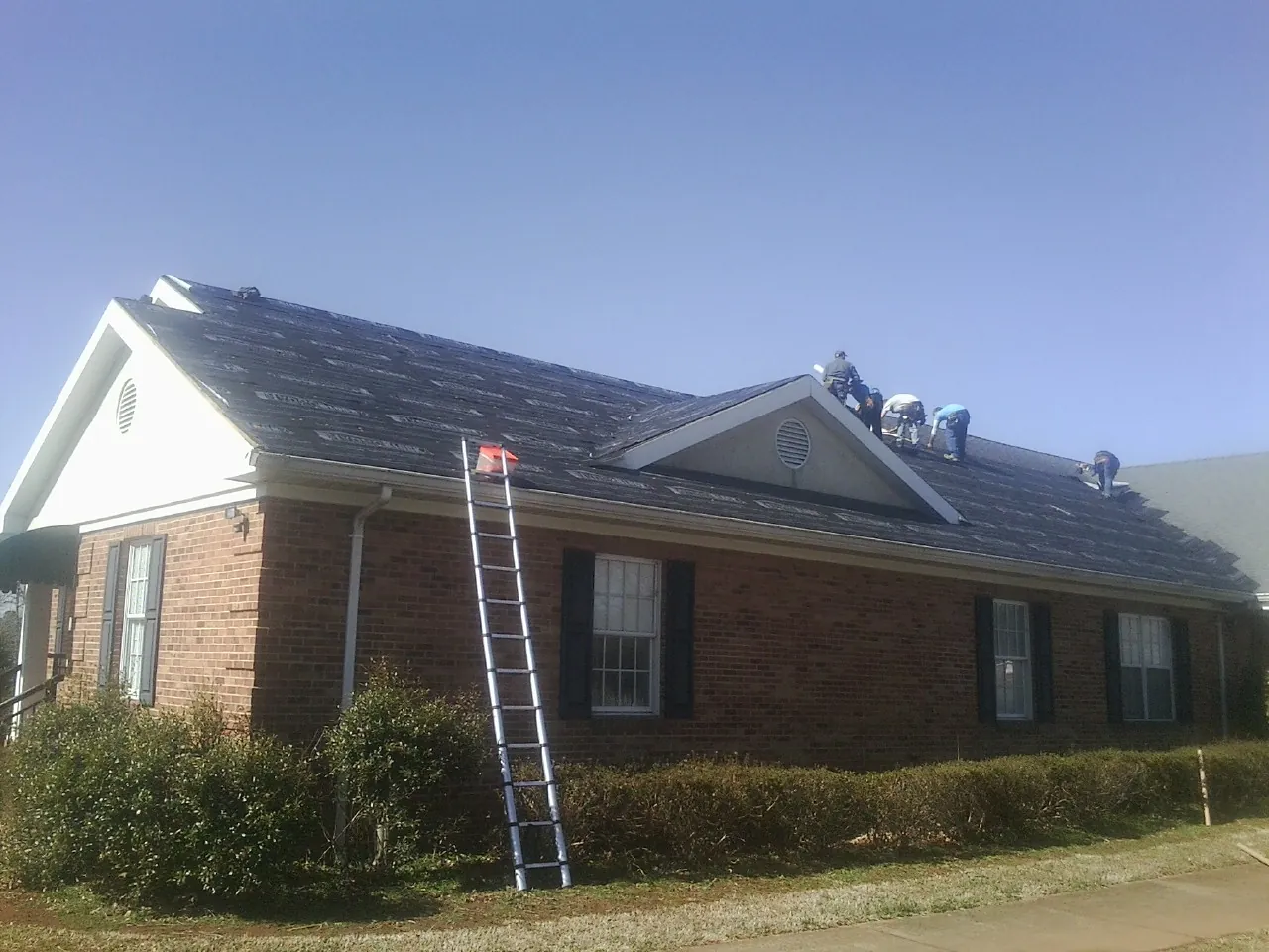 Crew tearing shingles off a brick ranch roof with a ladder set — Emergency Roof Repair work by our crew in Hammett