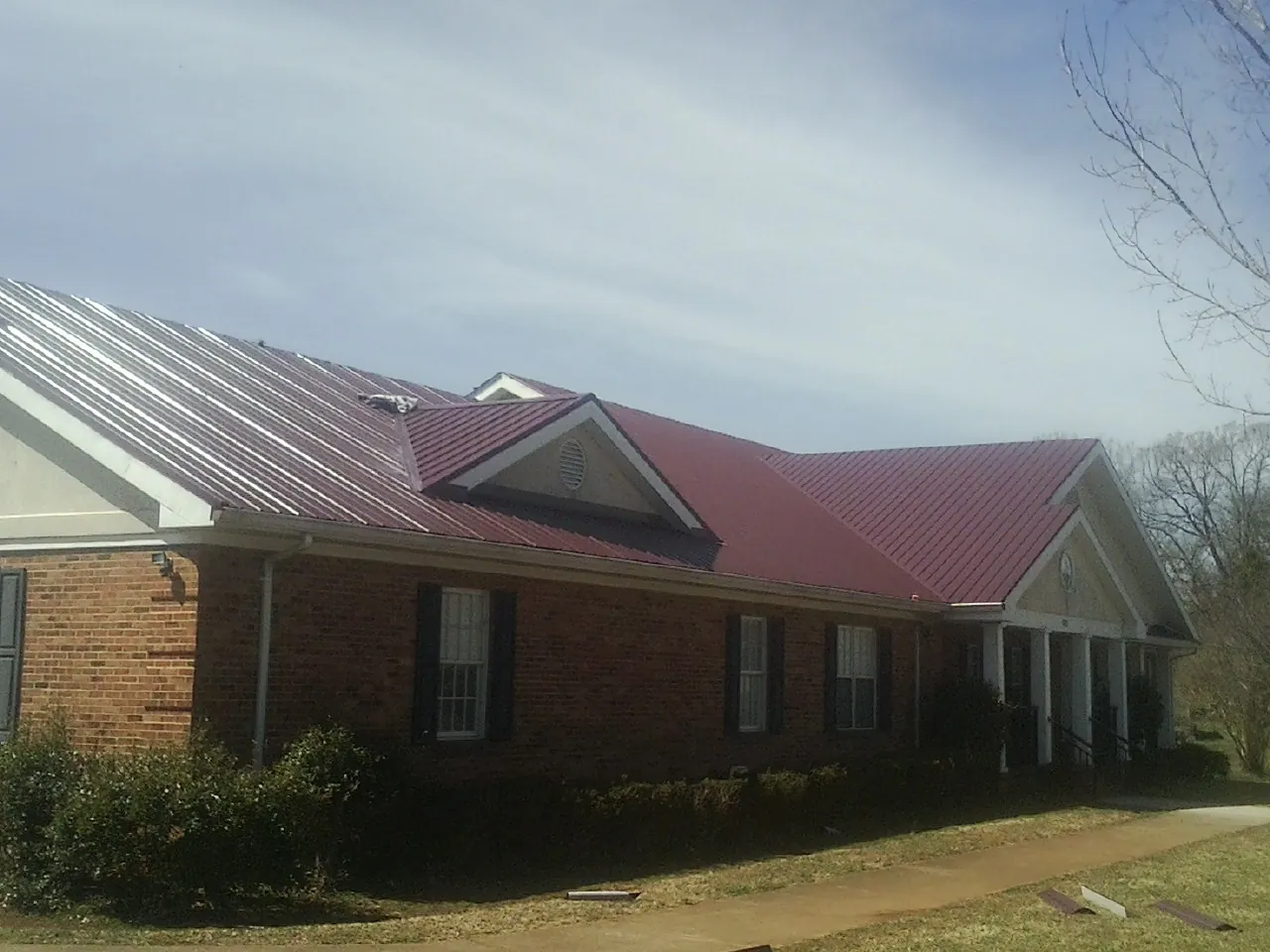 Red metal roof with gabled entries on a long brick building, from a Hail Damage Roof Repair job in Hammett