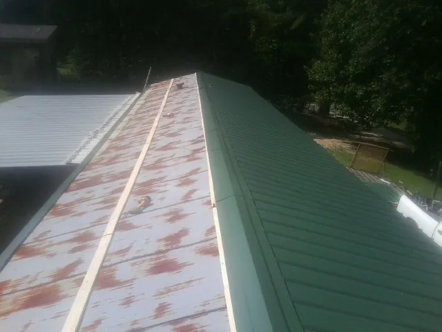 Old rusted panels beside newly installed green metal roofing — Wind Damage Roof Repair by Roofing Brothers in Hammett