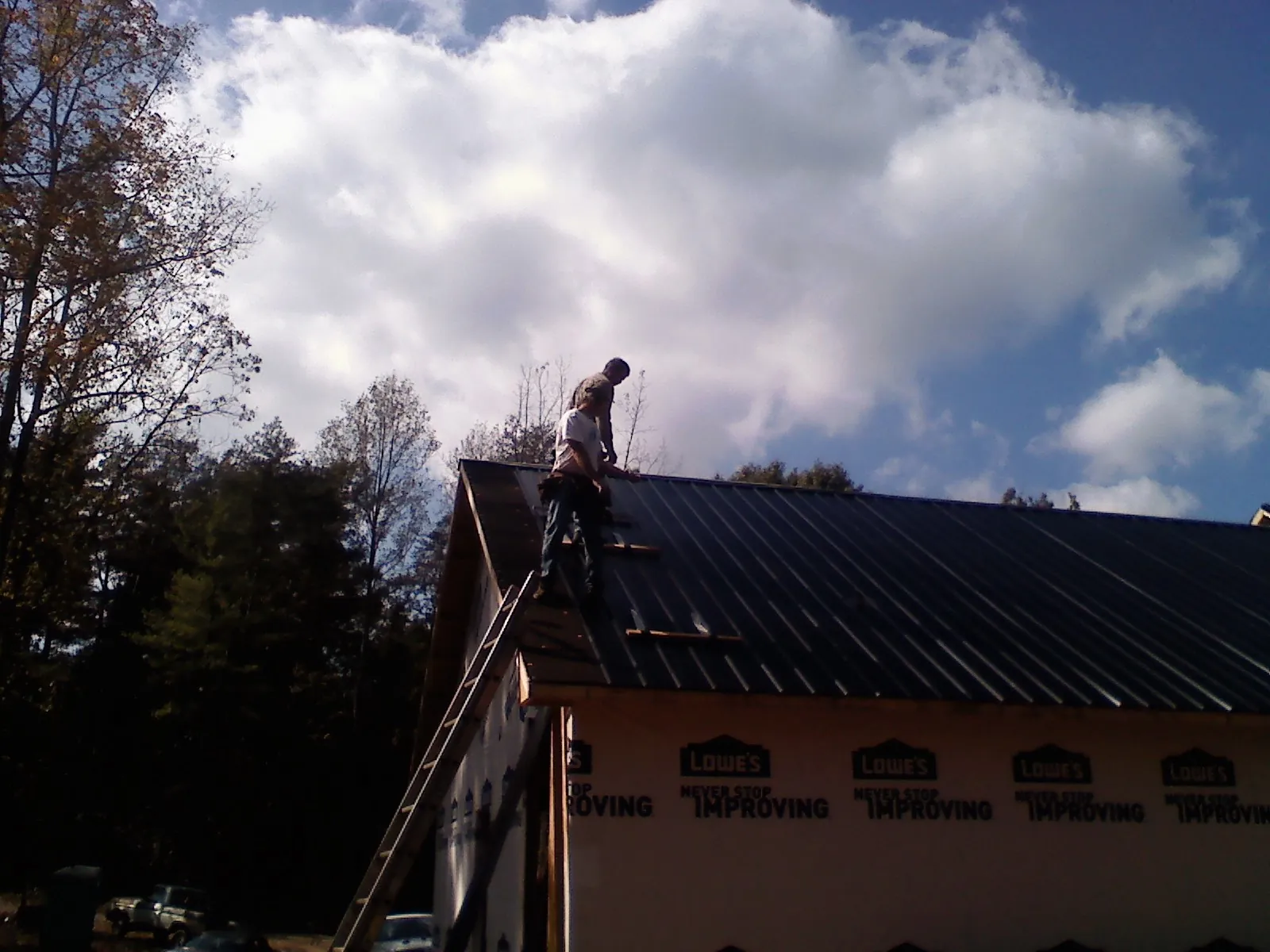 Roofer fastening dark metal panels high against a cloudy sky, from a Roof Inspection job in Hammett