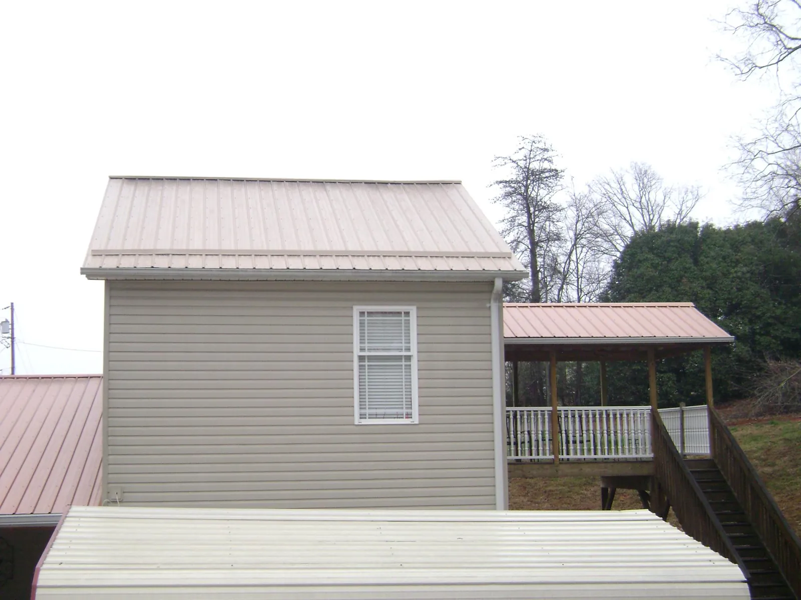 Tan metal roofs on a two story addition and attached porch, from a Roof Replacement job in Hammett